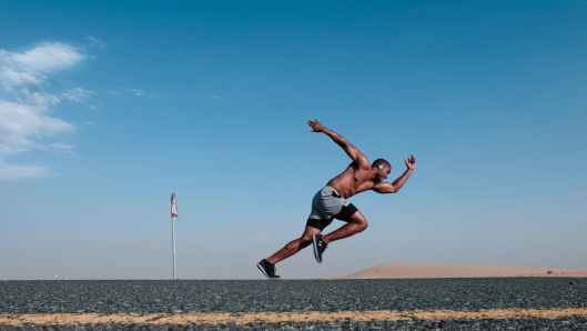 topless man wearing grey and black shorts sprinting on concrete road
