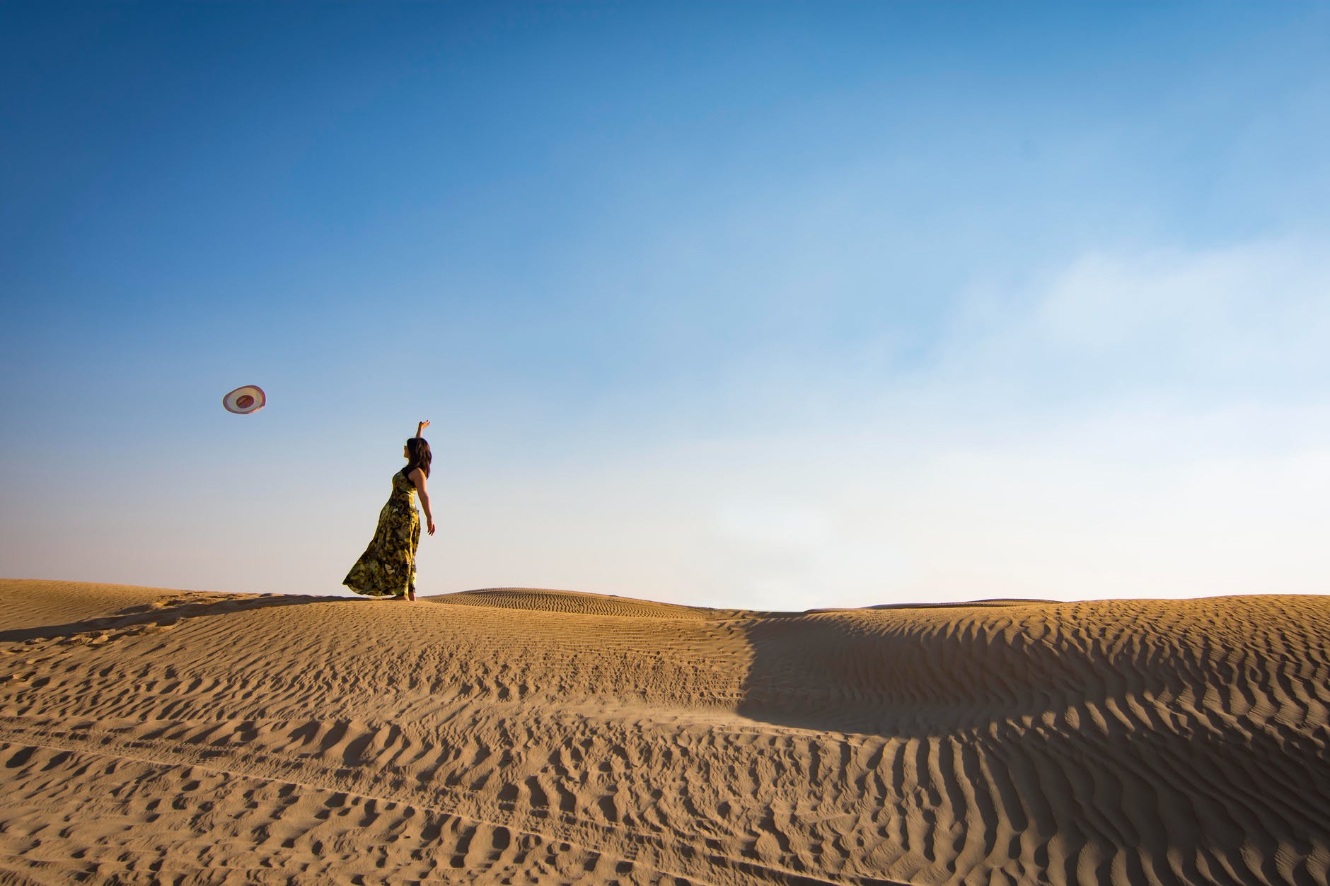 woman standing on sand dune throwing hat