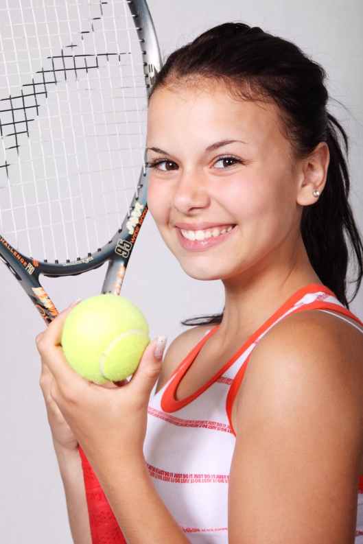 girl in white and orange stripe tank top holding black tennis racket