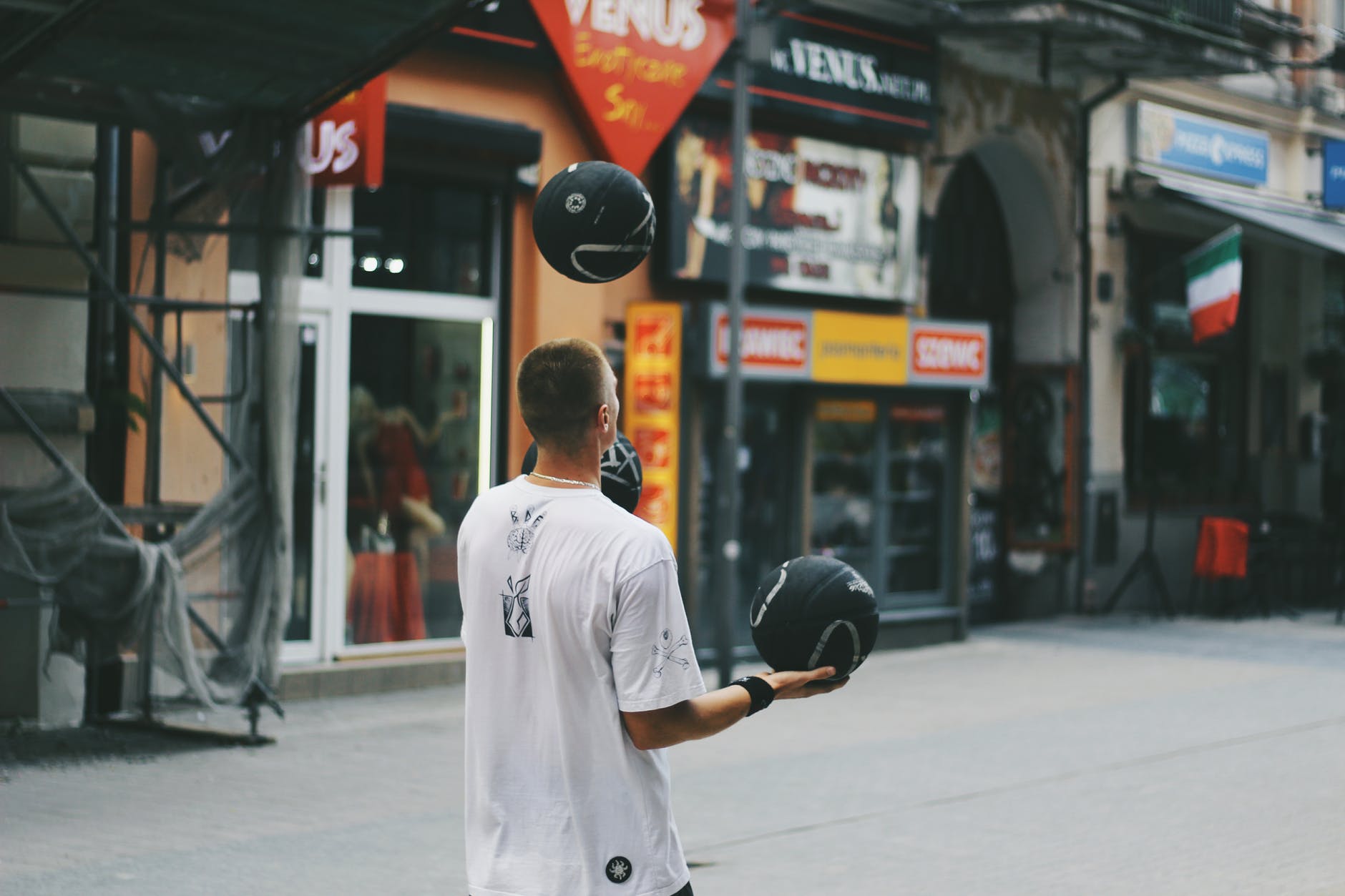 man juggling basketballs near storefront