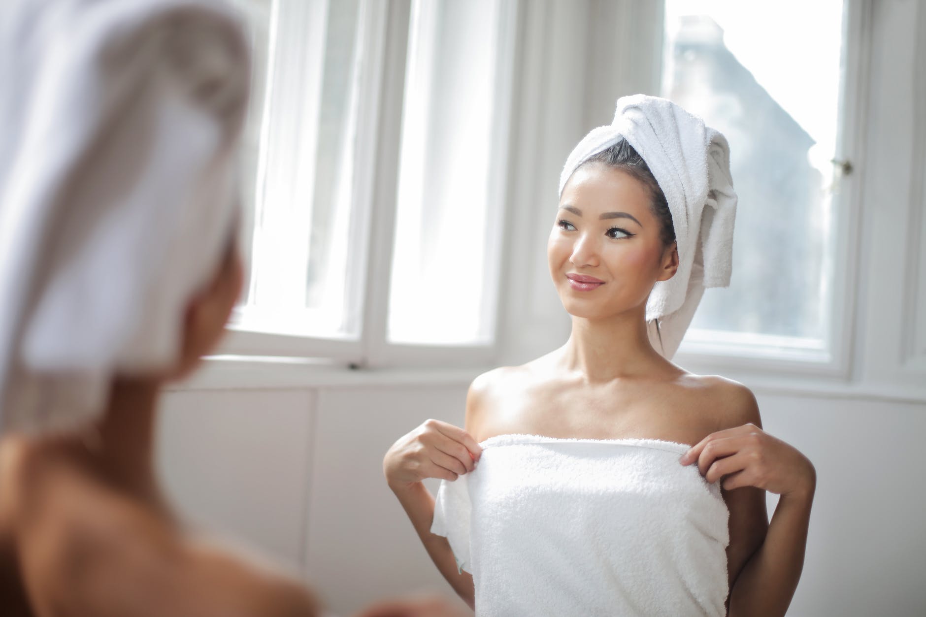 woman in white towel standing in front of the mirror