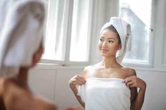 woman in white towel standing in front of the mirror